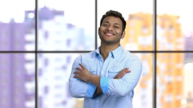 Koyu tenli, kolları katlanmış, dişleriyle gülümseyen genç bir adamın portresi..