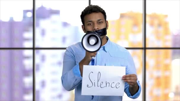 Mörkhyad aktivist med tejpad mun som försöker tala i megafon. — Stockvideo