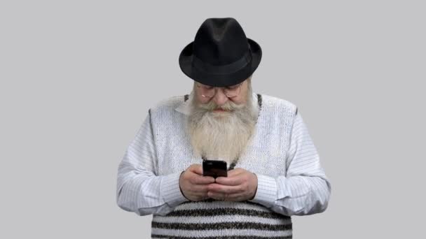 Old retired bearded man typing message on his smartphone. — Stock Video