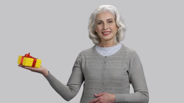 Alte Rentnerin mit grauen Haaren hält Geschenkbox. — Stockvideo