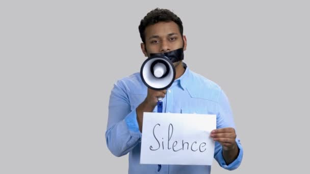 Dark-skinned man speaking in megaphone with taped mouth. — Stock Video