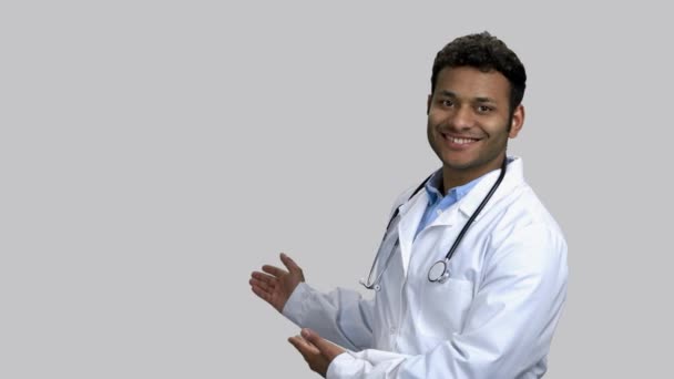 Young dark-skinned doctor pointing back at copyspace. — Stock Video