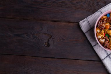 Kahverengi ahşap masayı ve kâsenin yarısını çikolatalı patlamış mısırla kapat..