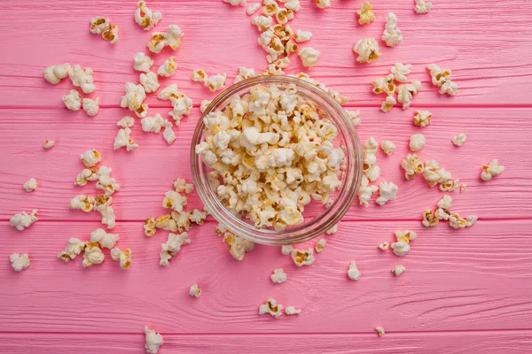 Flach legte Popcorn in eine Glasschüssel und streute Popcorn darauf auf rosa Hintergrund. — Stockfoto