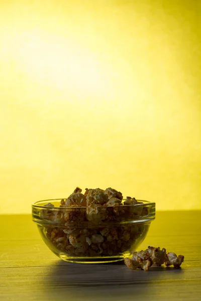 Sabrosas palomitas de maíz en tazón de vidrio sobre fondo amarillo . — Foto de Stock