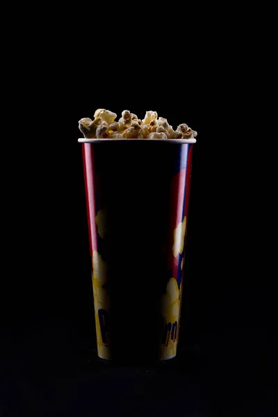 Copa de papel con sabrosas palomitas de maíz sobre fondo negro . — Foto de Stock