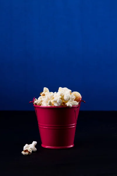 Červený kbelík plný popcornu na tmavomodrém pozadí. — Stock fotografie