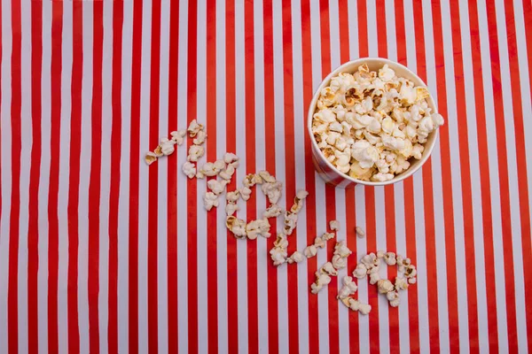 Palomitas de maíz en tazón y palomitas de maíz arregladas en palabra de película sobre fondo rojo blanco . — Foto de Stock