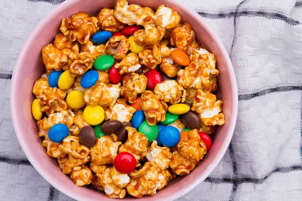 Chocolate candies and golden popcorn mix in ceramic plate on white napkin. — Stock Photo, Image