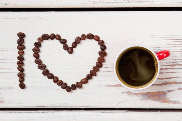 Rote Tasse Kaffee und Bohnen in Herzform angeordnet. — Stockfoto