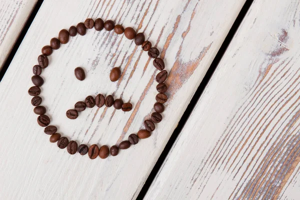 Unhappy coffee bean smiley face on white wood.