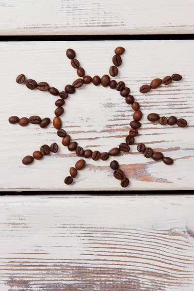 Kávová zrna ve tvaru slunce na bílém dřevě. — Stock fotografie