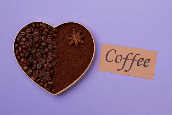 Coração de grãos de café e pó no fundo roxo . — Fotografia de Stock