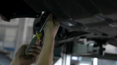 İşçi Tamircisi kaldırılmış arabanın altında otomobillerin vidalarını söküyor.