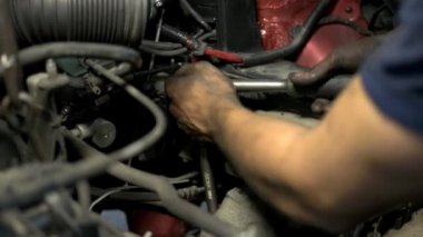Kirli elli tamirci, İngiliz anahtarıyla arabanın motor detaylarını vidalamaya çalışıyor..