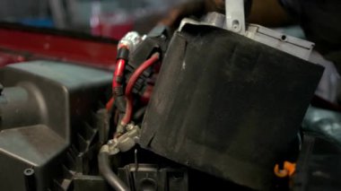 Araba servisi çalışanı bir araba motoruna akümülatör yüklüyor.