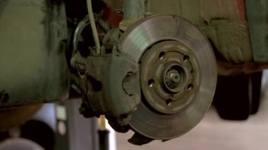 Tamirci kaldırılmış bir arabanın tekerleğini kuruyor ve vidalıyor..