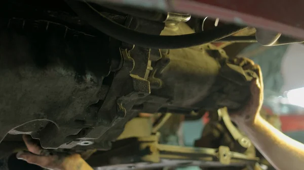 Рабочий механик откручивает части автомобиля снизу под поднятым автомобилем . — стоковое фото