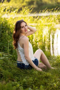 Güzel kız beyaz bir tişört ve kot şort nehir kenarında oturur