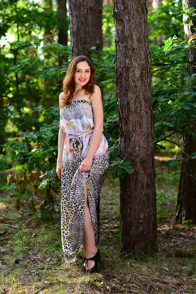 Vackra unga leende kvinna poserar i lång klänning utomhus — Stockfoto