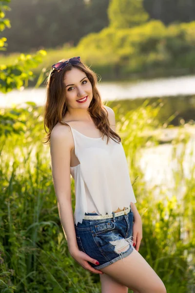 Mooi meisje in een wit overhemd en denim shorts staande in de buurt van het meer — Stockfoto