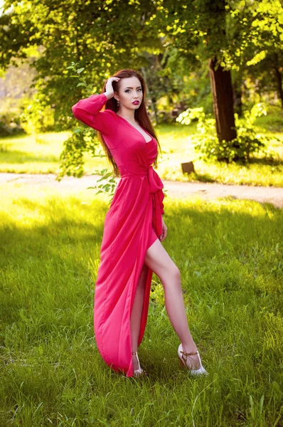 Привлекательная рыжая девушка, наслаждающаяся природой. Красивая молодая женщина в длинном красном платье — стоковое фото
