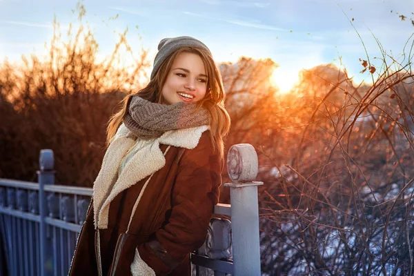 Joyeux joyeux fille en manteau marchant dans la rue par une froide soirée d'hiver au coucher du soleil — Photo