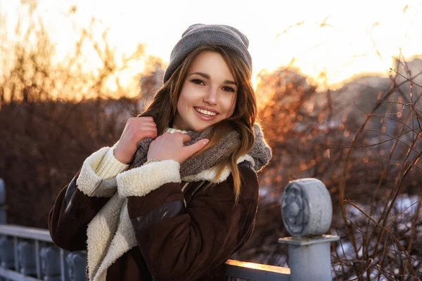 Счастливая девушка в пальто, идущая по улице холодным зимним вечером на закате — стоковое фото