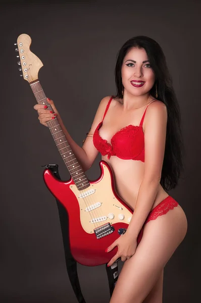 Sexy jonge brunette in rode lingerie houden van elektrische gitaar in studio — Stockfoto