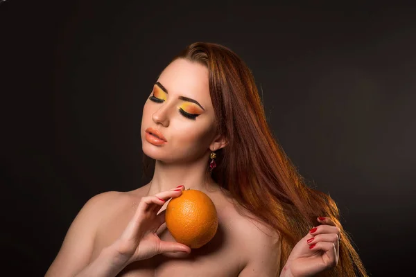 Привлекательная молодая женщина держит оранжевый с косметикой — стоковое фото