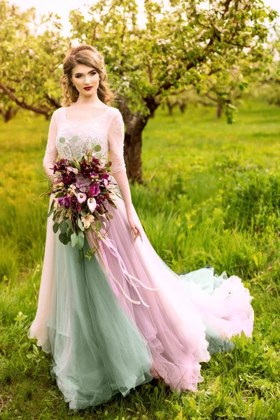 Lüks gelinlik kırmızı dudaklar makyaj ve uzun dalgalı saç modeli ile güzel genç gelin kadın. Yeşil park, açık fotoğraf poz çekici kız portre.