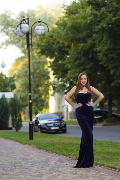 Moda mulher de cabelo vermelho posando sexy, vestindo vestido de noite azul longo na rua da cidade — Fotografia de Stock