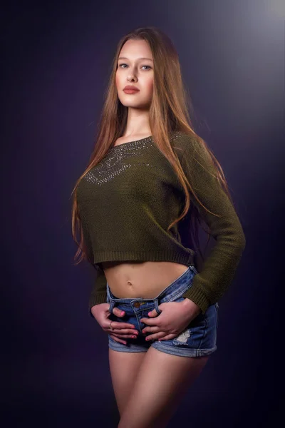 Glimlachend sexy vrouw met lange haren in blue jeans korte en grijze top poseren over donkere achtergrond — Stockfoto