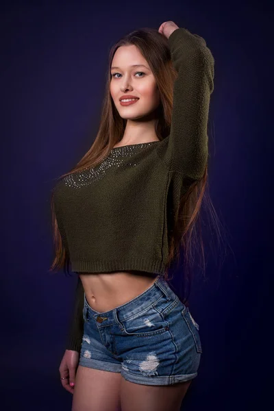 Sorrindo sexy fêmea com cabelos longos em jeans azul curto e cinza top posando sobre fundo escuro — Fotografia de Stock