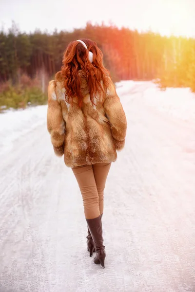 Invierno y recreación. Mujer joven de vuelta a la cámara caminando por el bosque, la libertad, disfruta escuchando música en los auriculares —  Fotos de Stock