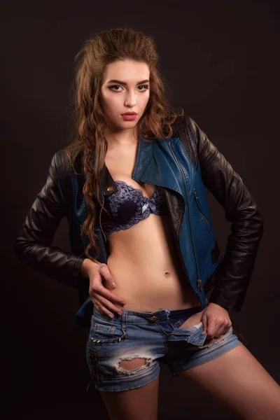 Séduisante fille portant un short en denim et une veste en cuir sur une lingerie bleue élégante. Prise de vue studio, portrait mode — Photo