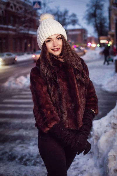 Fiatal szép boldog mosolygó lány pózol utcában este. Nézi a kamera modell. Nő visel elegáns téli ruhák — Stock Fotó