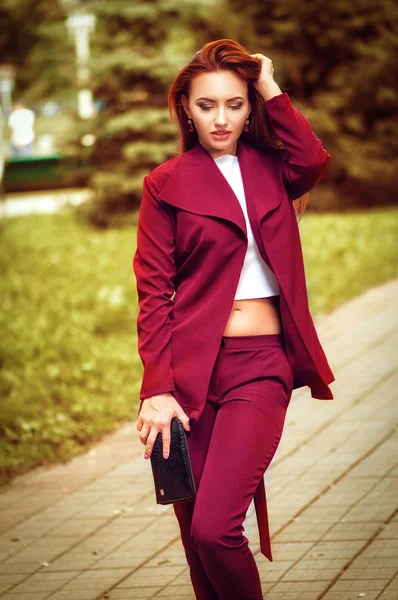 Vacker röd huvud ung kvinna klädd i röd jacka, skinnväska, promenad på gatan. Mode foto — Stockfoto