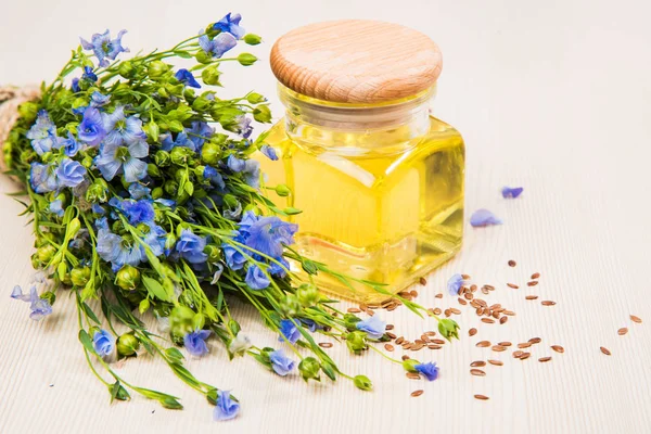 Leinöl, Leinsamen und Blumen auf hellem Hintergrund. — Stockfoto