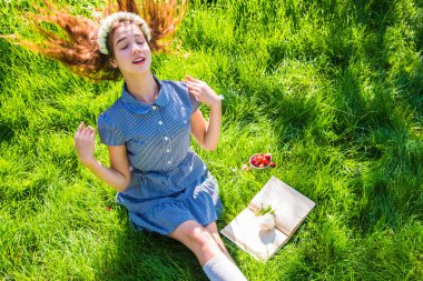 Kız parlak güneşli bir günde yeşil çimenlerin üzerine bir kitap okuma