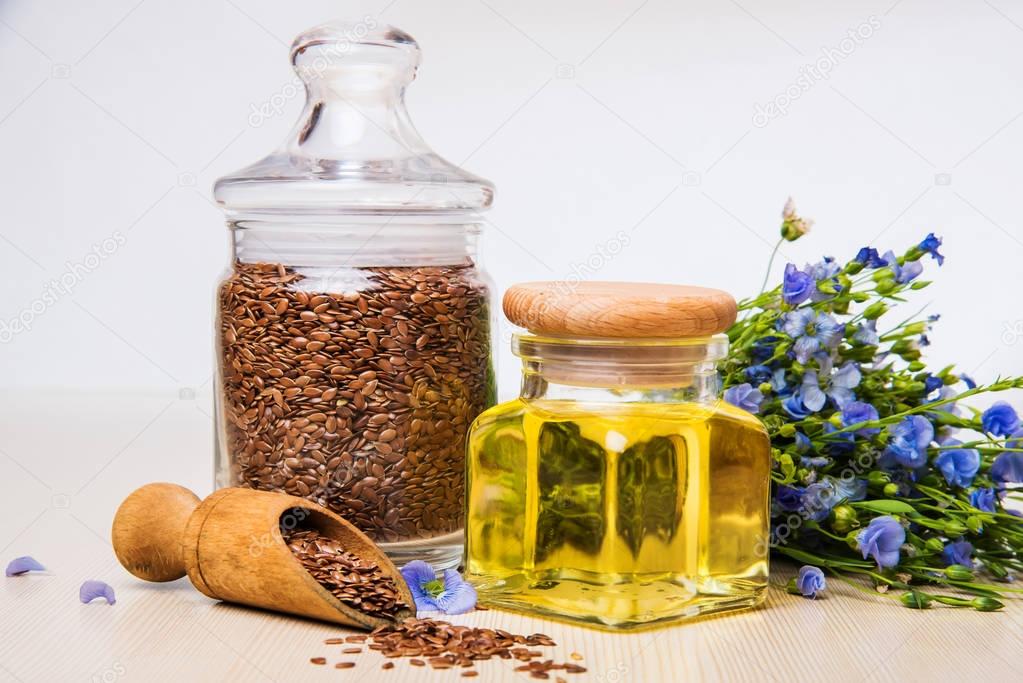 Linseed oil, flax seeds, and flowers on a light background.