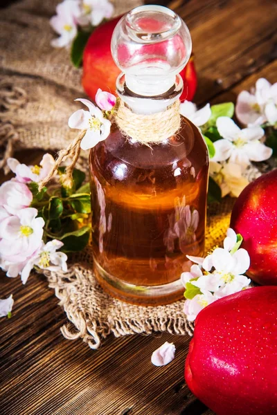 Uma garrafa de vinagre de maçã (cidra), maçãs frescas e flores de macieira em um fundo de madeira. Estilo de país . — Fotografia de Stock
