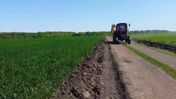 Le tracteur longe la route parmi les champs de blé jeune — Video
