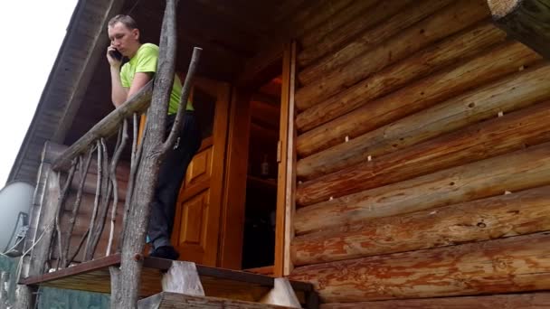 Jonge man op een houten terras praten aan de telefoon — Stockvideo