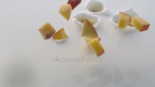 Pfirsichstücke fallen mit Spritzern in weißen Joghurt — Stockvideo