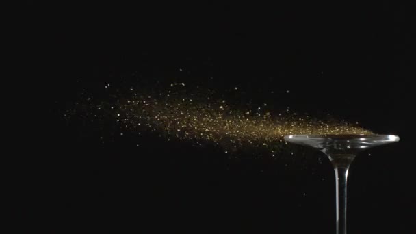 空中を舞う黄金の輝きが スローモーションでガラスから吹き飛ばされる黒を基調とした祝賀会とマジックのコンセプト — ストック動画