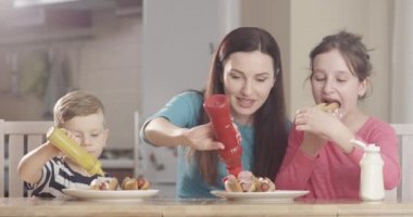Mutfak masasında Hotdog pişirirken Anne, Oğlu ve Kızıyla Eğlenirken Kırmızı Kamera 'yı çekmiş.