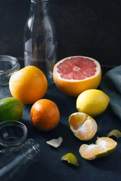 Citrus mix with empty glass bottle on the dark stone background