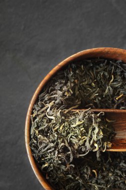 Karanlık taş zemin üzerine ahşap kase dikey çay yaprakları