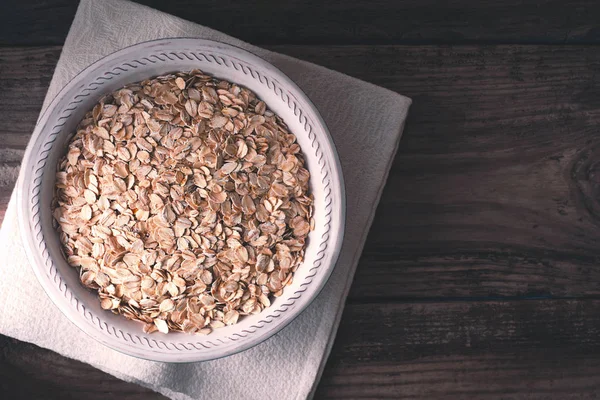 Copos de avena crudos en el tazón en la vista superior de la mesa de madera —  Fotos de Stock